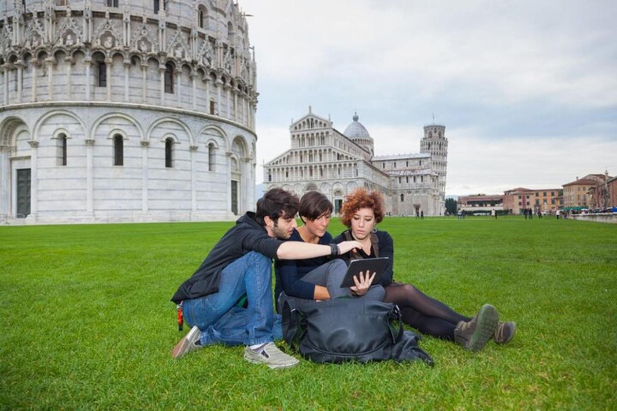 tre persone sedute sull'erba davanti alla torre pendente