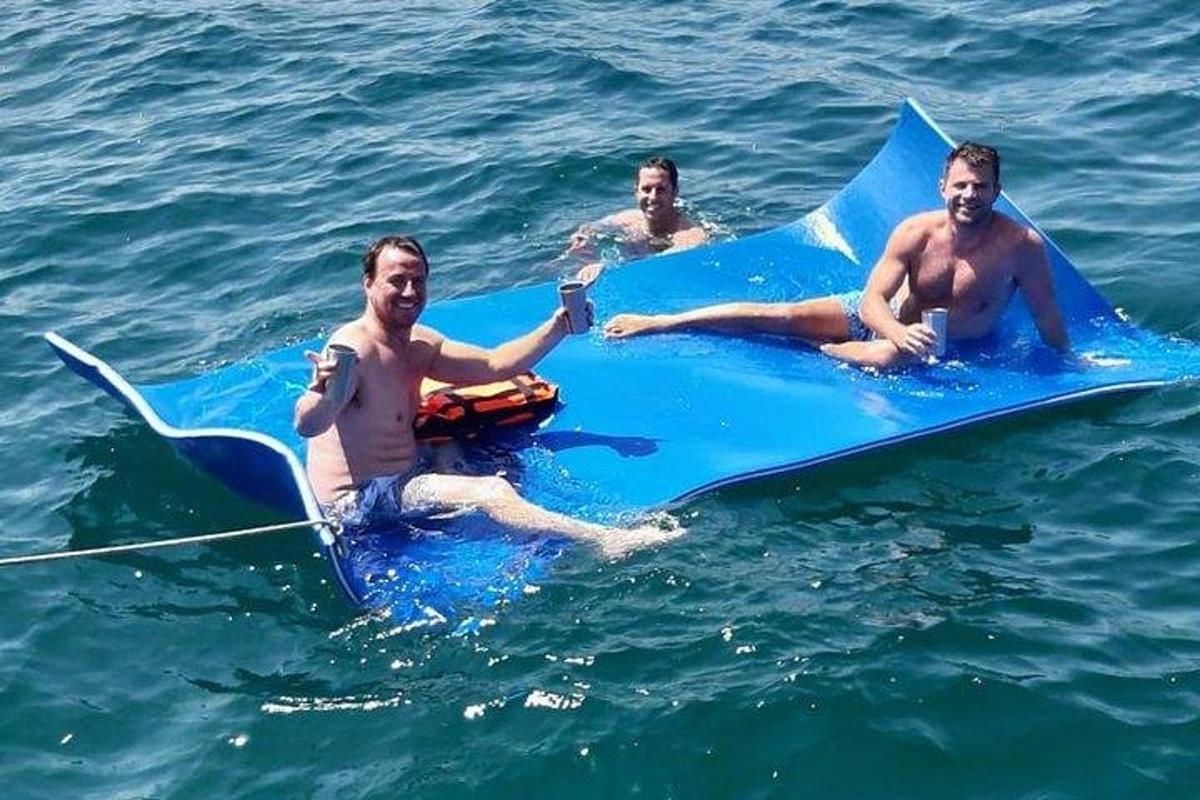 drei Männer liegen auf einem blauen Surfbrett im Wasser