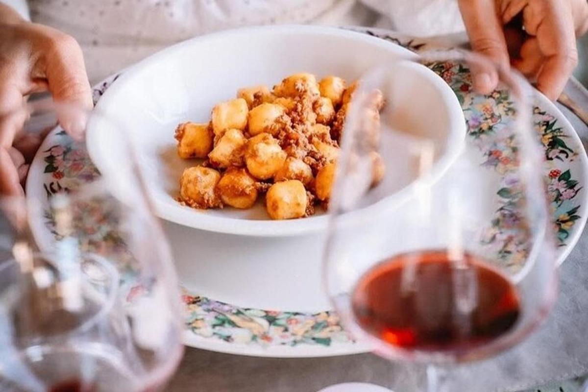 a person holding a bowl of food and a glass of wine