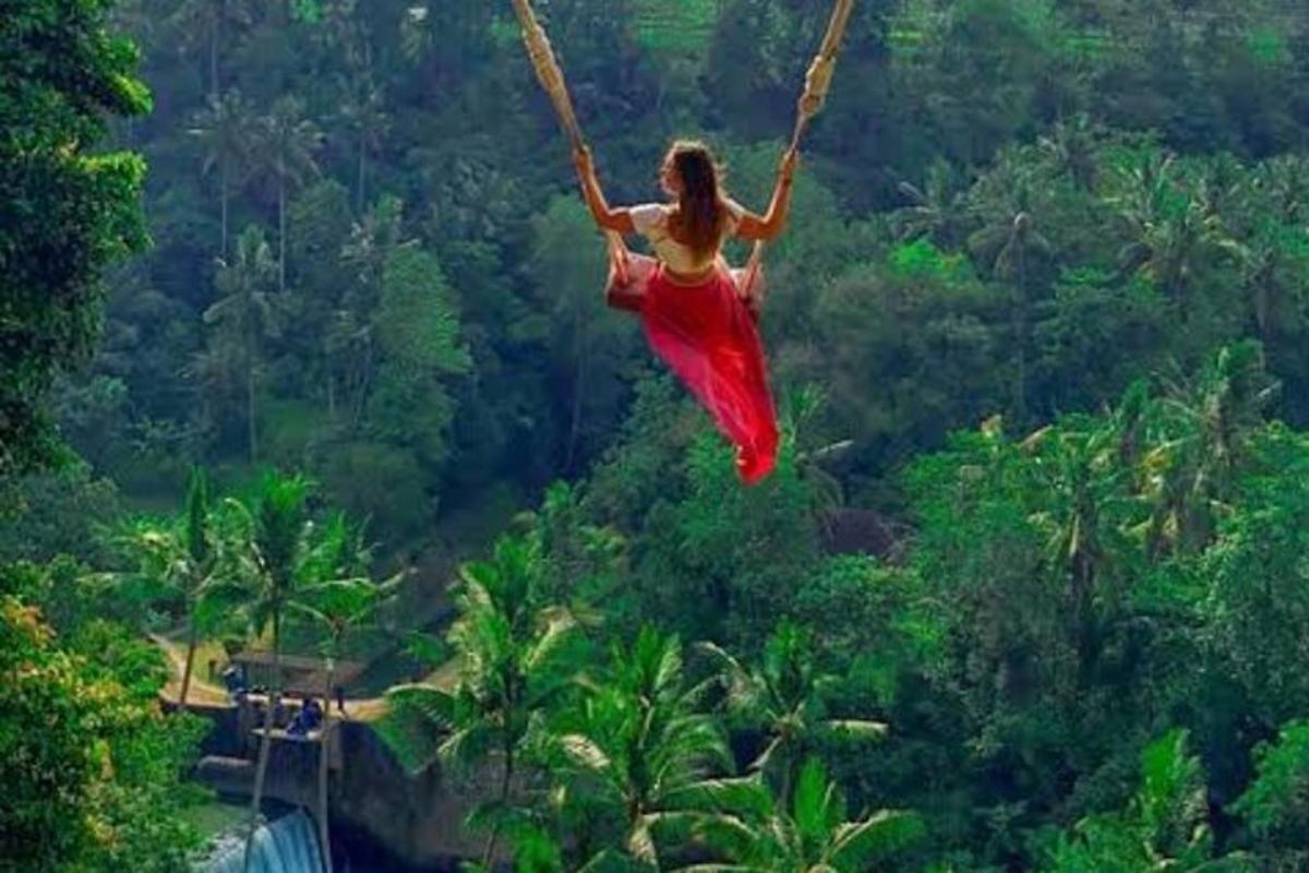 a woman in a red dress swinging on a rope swing