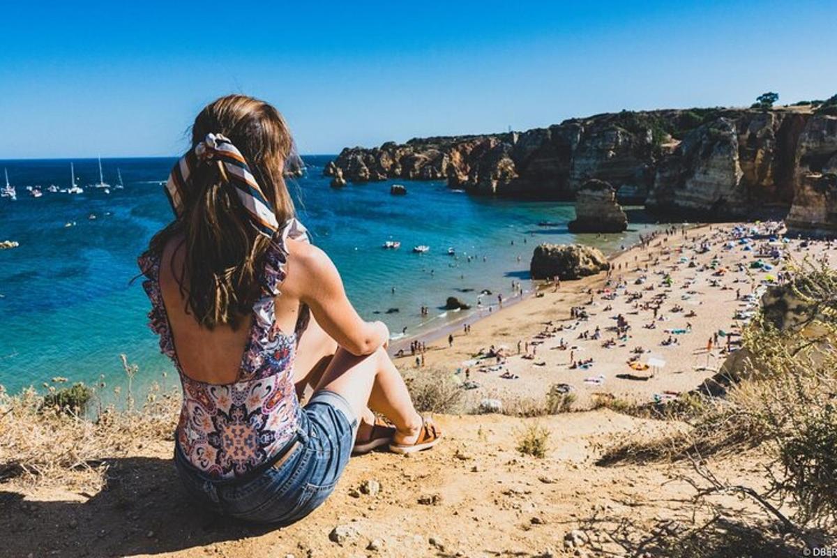 a woman sitting on a cliff looking at a beach