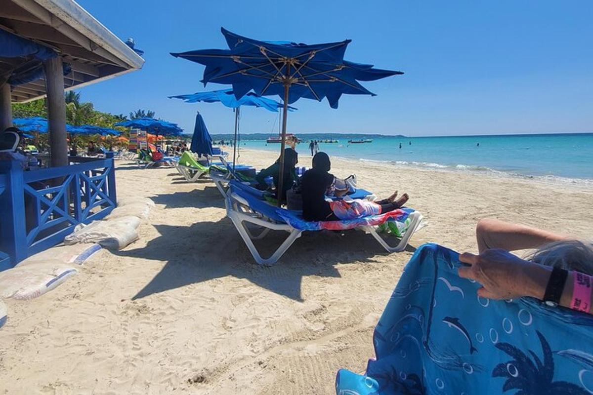 eine Gruppe von Menschen sitzt auf Stühlen unter einem Sonnenschirm am Strand
