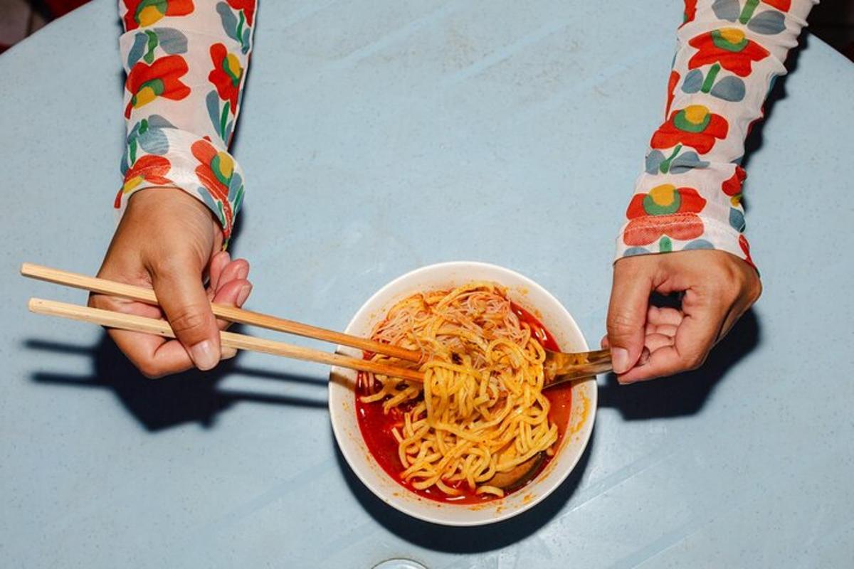 a person holding a bowl of noodles with chopsticks