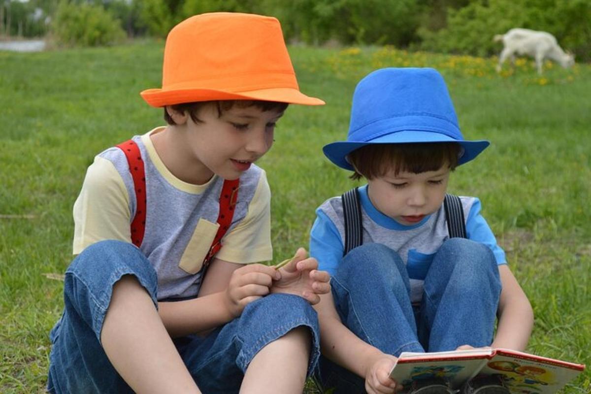 dva mladí chlapci sedí na trávě a čtou si knihu