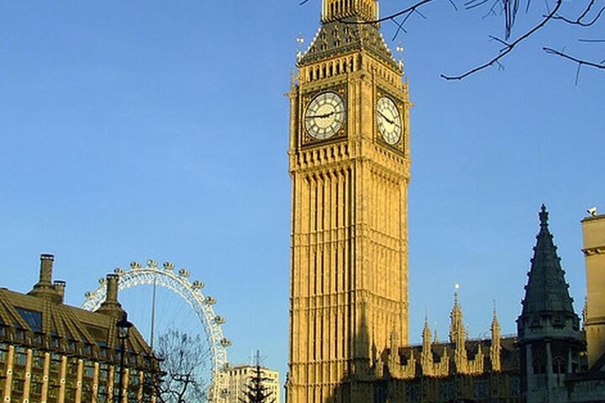 Una alta torre de reloj con el London Eye al fondo
