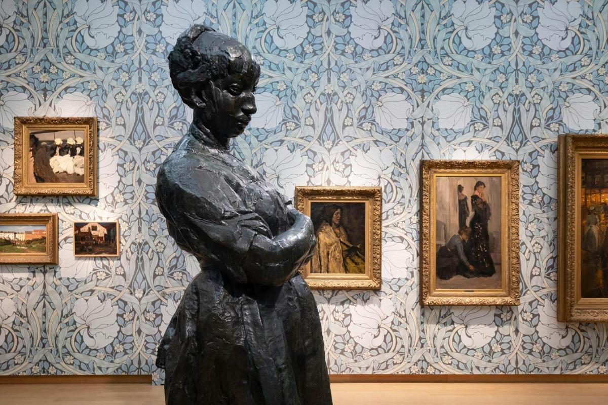 a statue of a woman in front of a wall with paintings