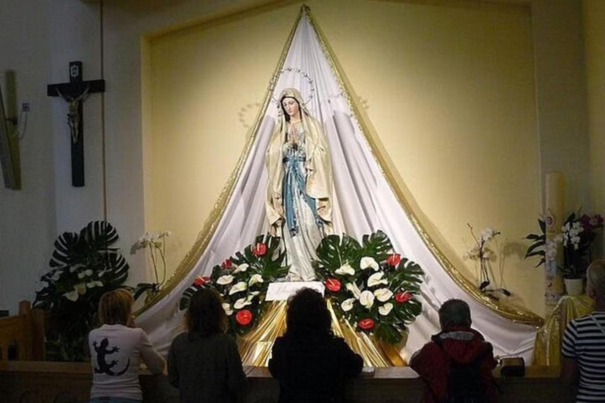 Un grupo de personas en una iglesia mirando una pintura de una mujer.