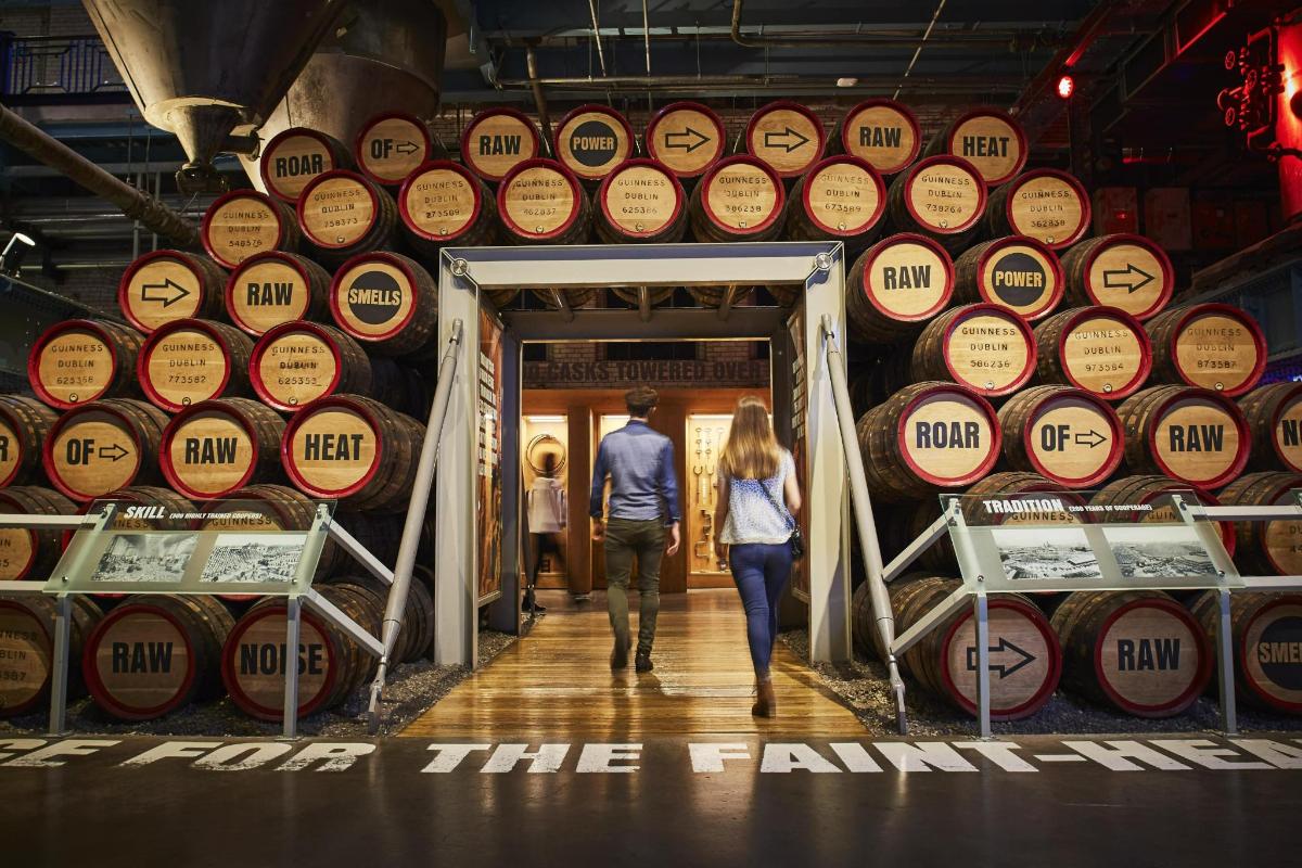 a man and woman walking through a room filled with wine barrels