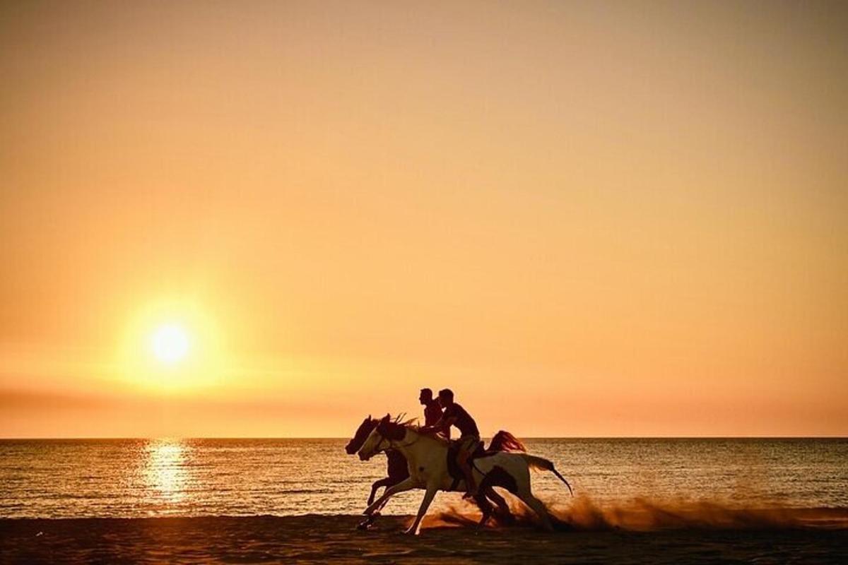 Dos personas montando a caballo en la playa al atardecer