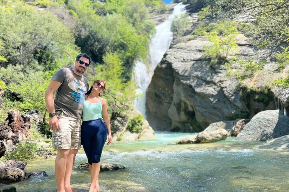 um homem e uma mulher parados em um rio com uma cachoeira