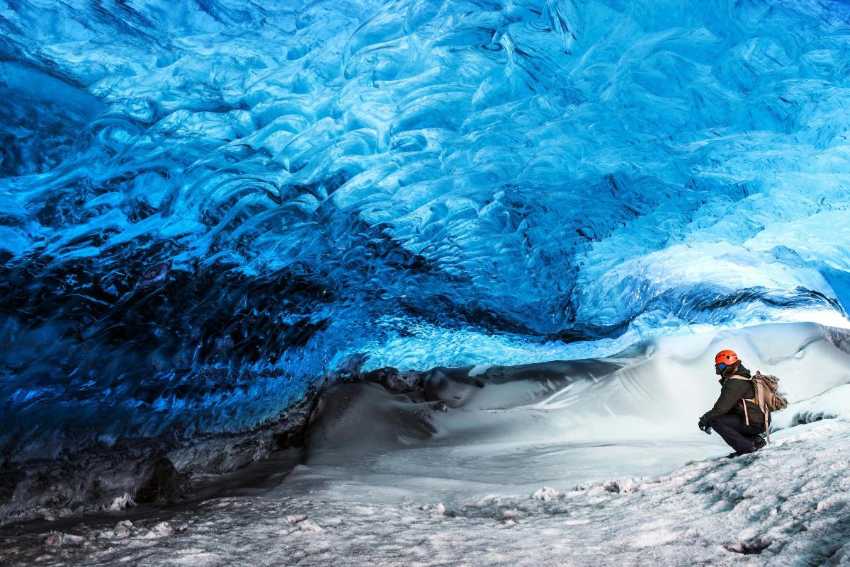 Una persona se encuentra frente a una cueva de hielo azul.