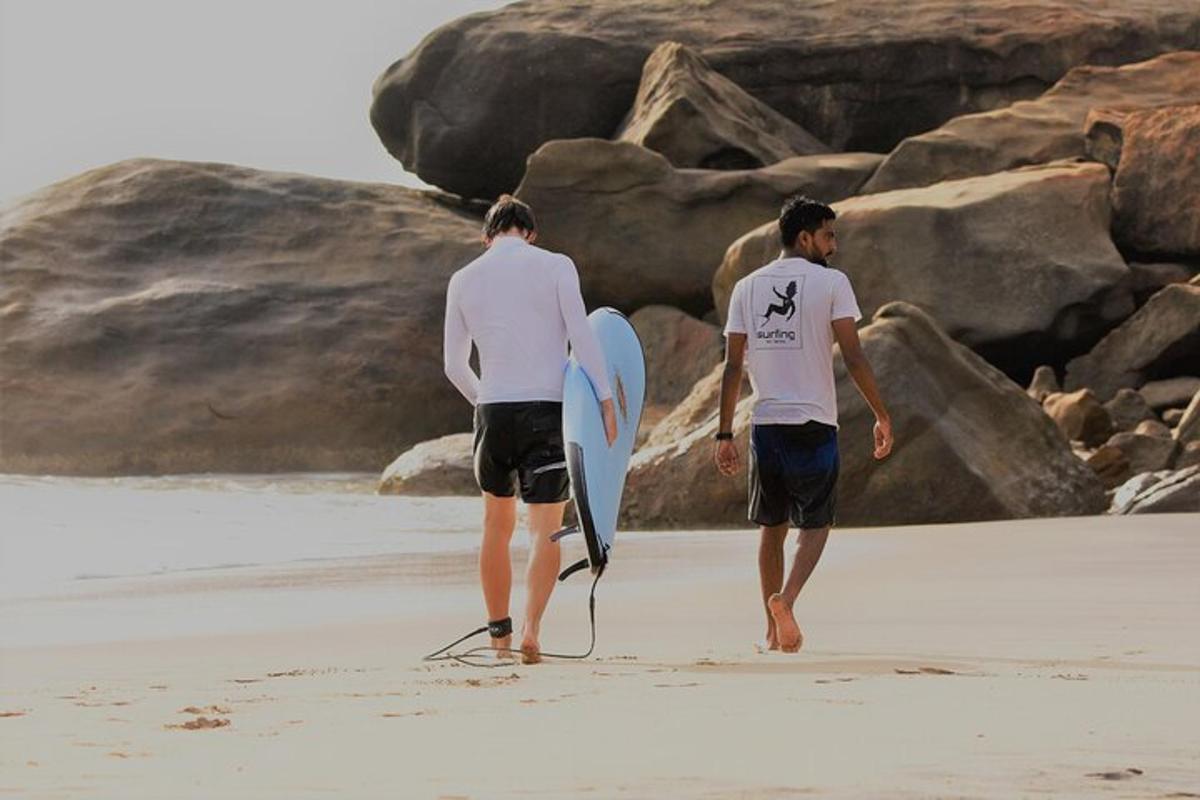 dos homes caminant per la platja amb una taula de surf