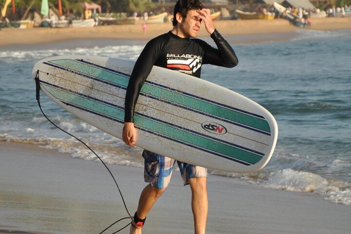 un home caminant per la platja sostenint una taula de surf