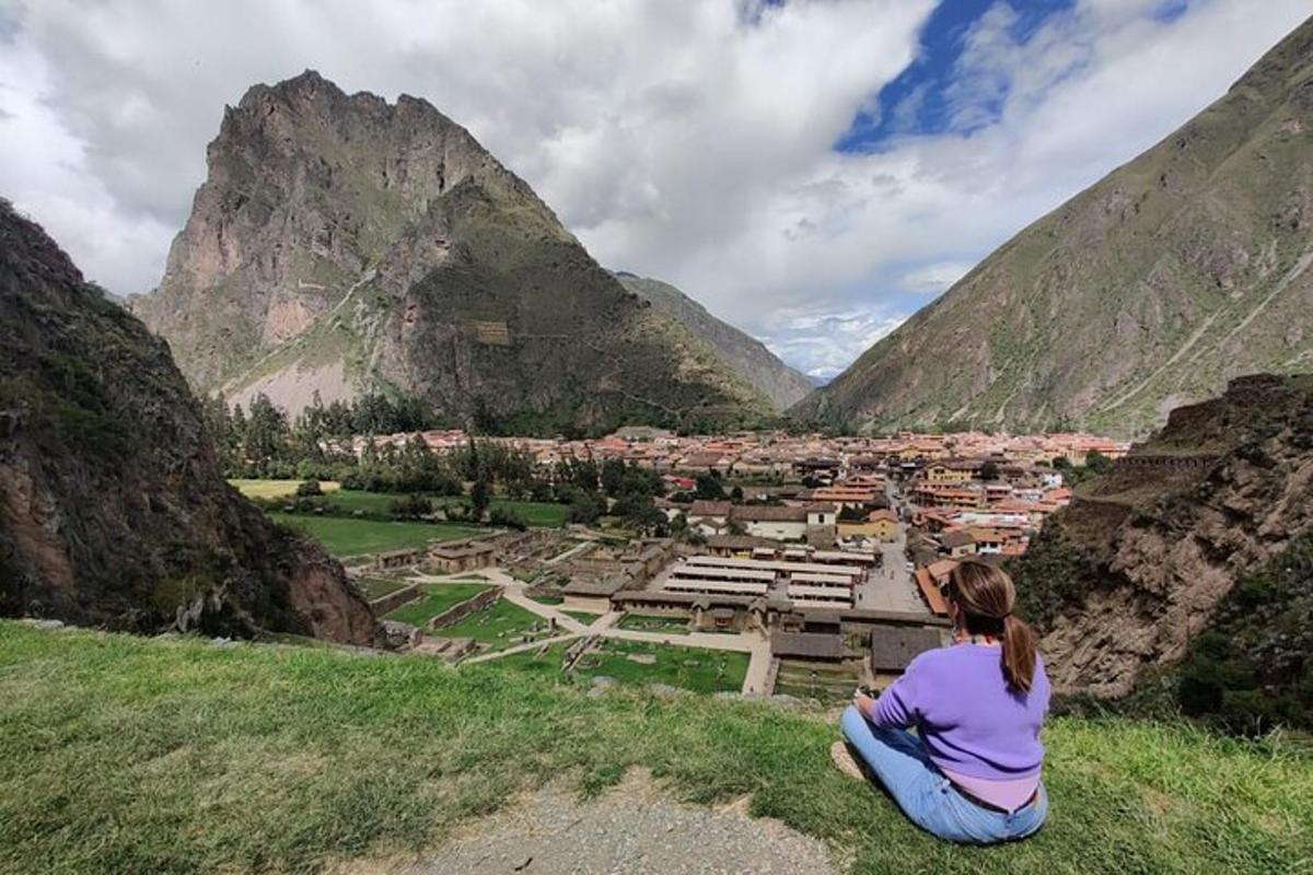 a woman sitting on a hill looking at a village in the mountains