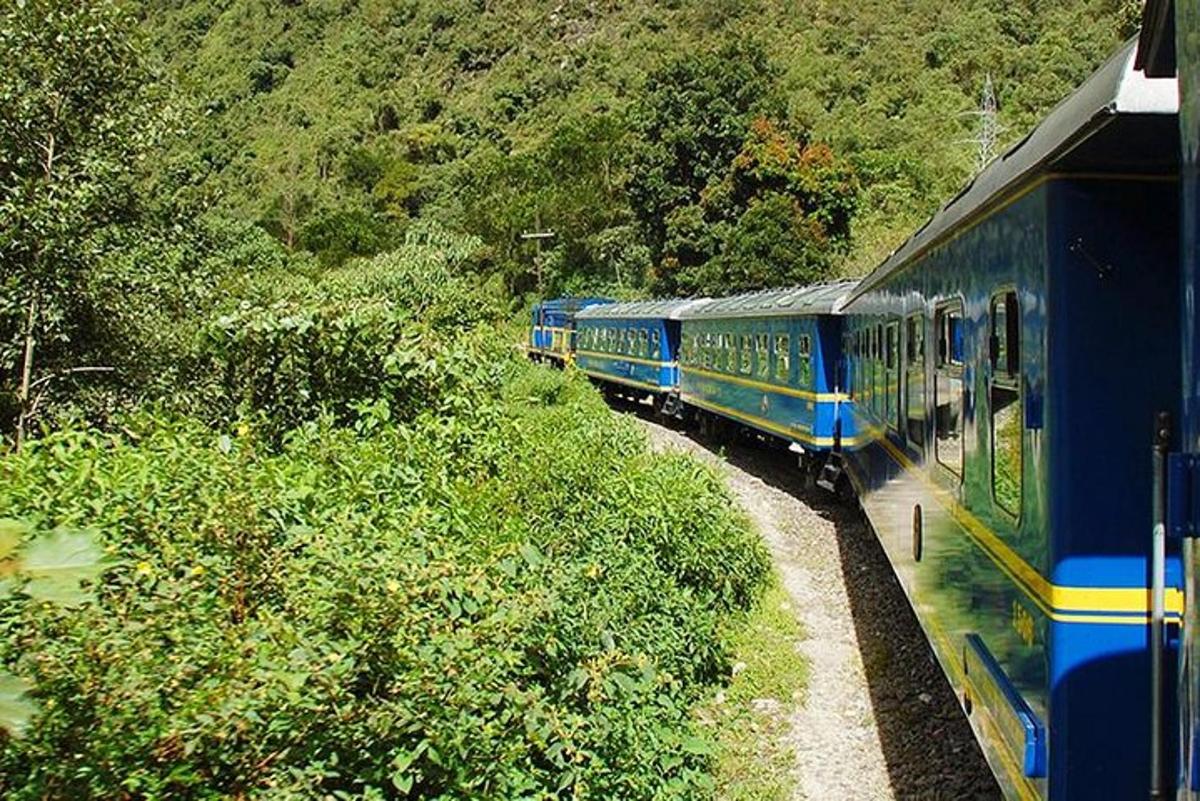 một đoàn tàu màu xanh đang chạy dọc theo đường ray bên cạnh một ngọn núi