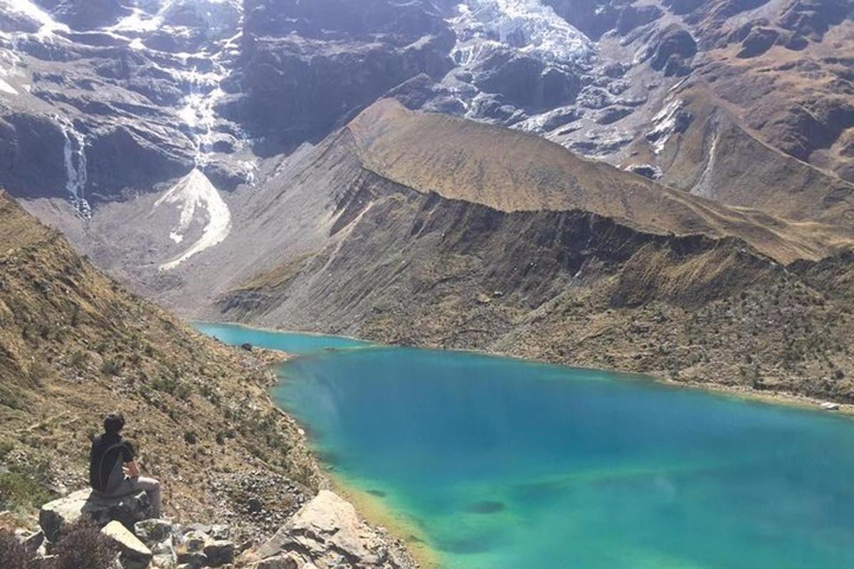 Un hombre sentado en la ladera de una montaña con vistas a un lago azul.