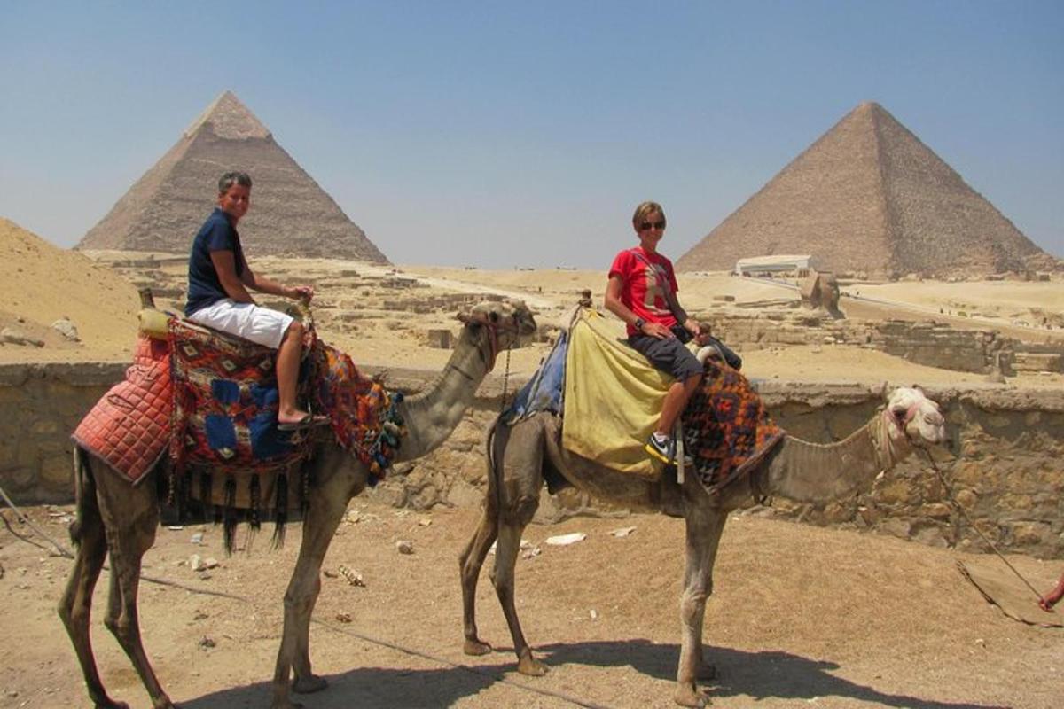 deux hommes à dos de chameau devant les pyramides