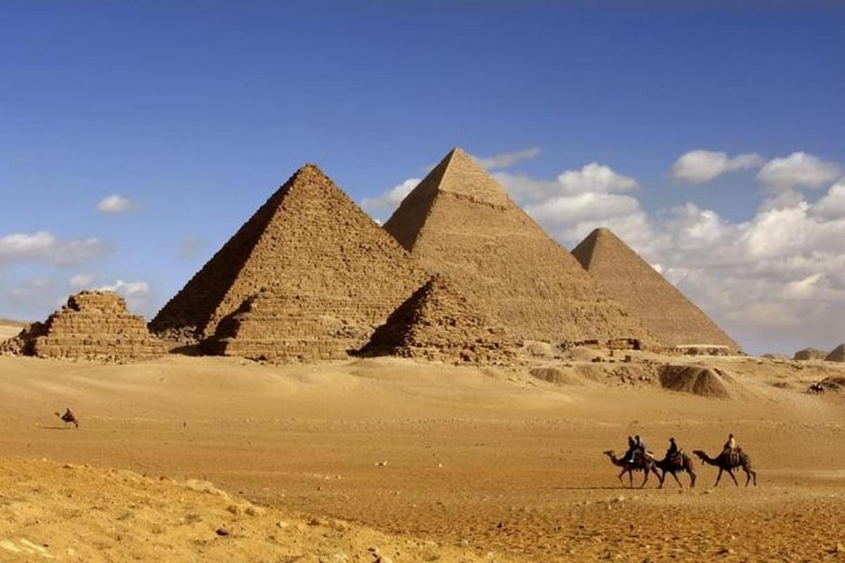 a group of people riding camels in front of pyramids