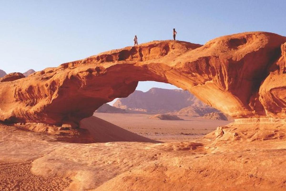 two people standing on top of an arch in the desert