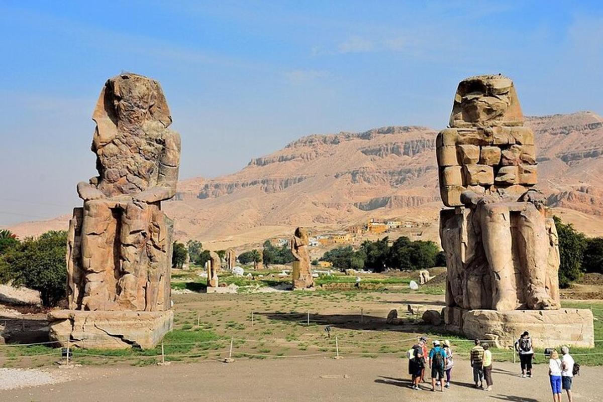 Un grupo de personas caminando cerca de dos grandes estatuas de piedra.