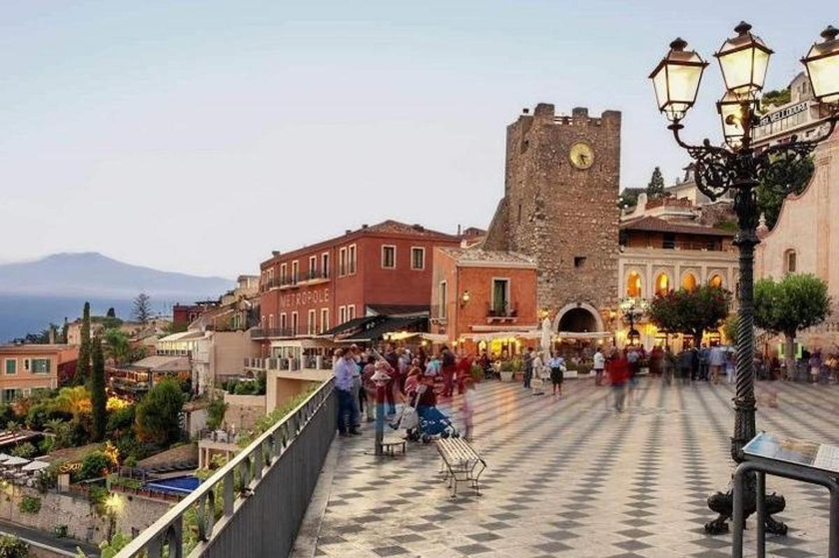 un gruppo di persone che camminano in una città con una torre dell'orologio