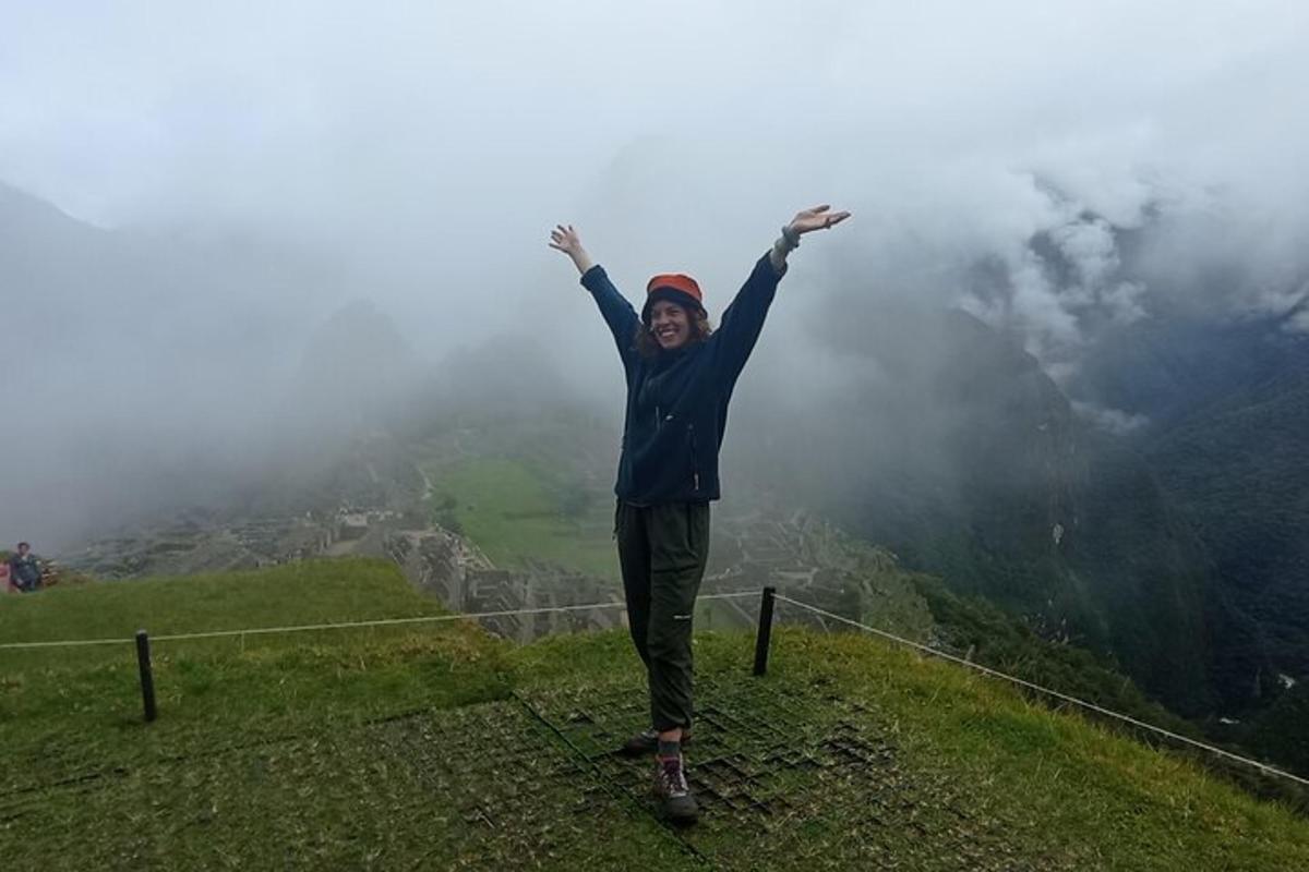 Una mujer parada en la cima de una montaña con los brazos en alto.
