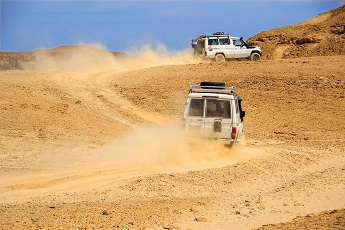 Dos vehículos circulando por un camino de tierra en el desierto.