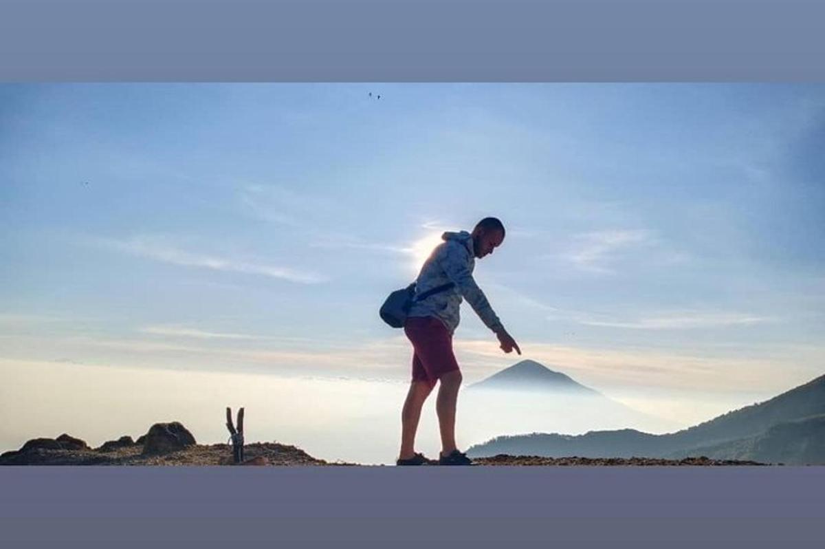 seorang wanita berdiri di atas bukit dengan latar belakang gunung