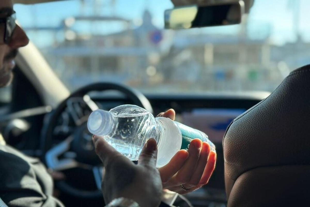 una persona seduta in macchina con in mano una bottiglia di plastica