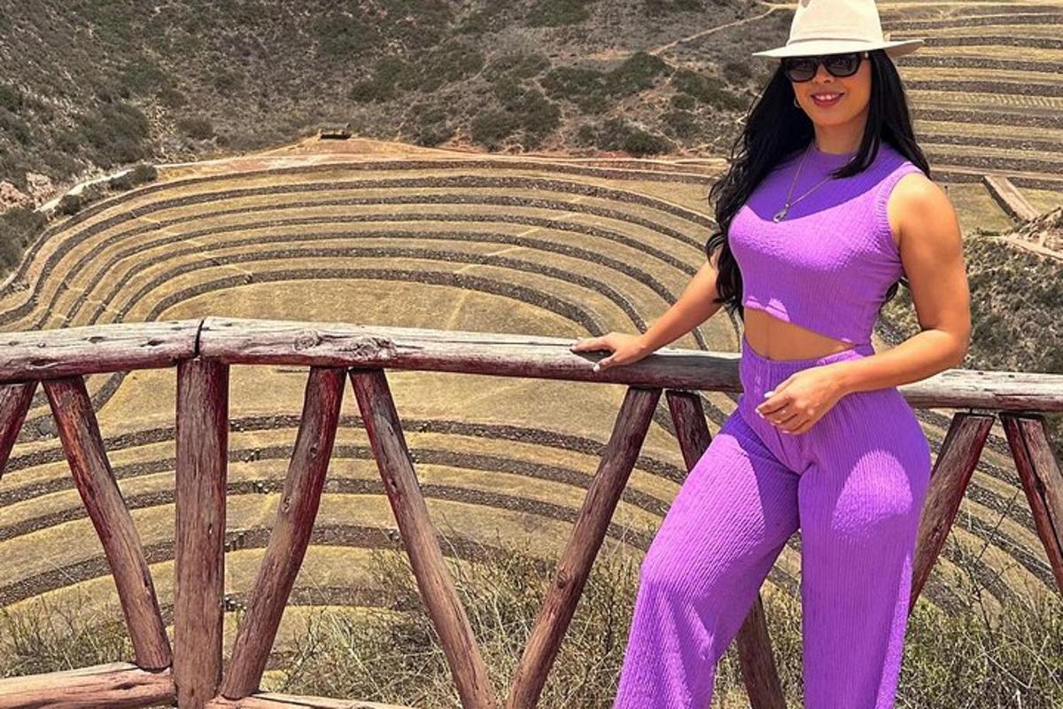 Una mujer con un vestido morado y un sombrero apoyada en una barandilla.