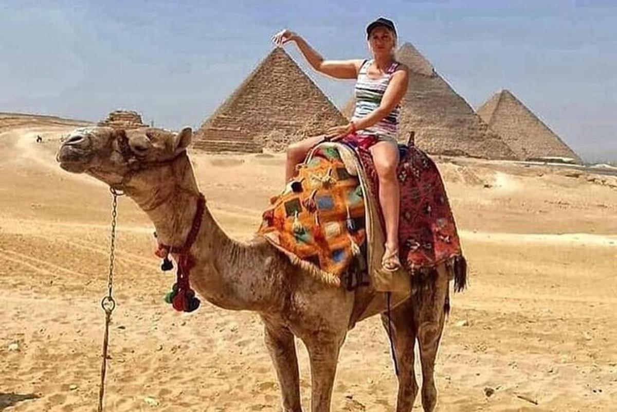 seorang wanita menunggang unta di hadapan piramid