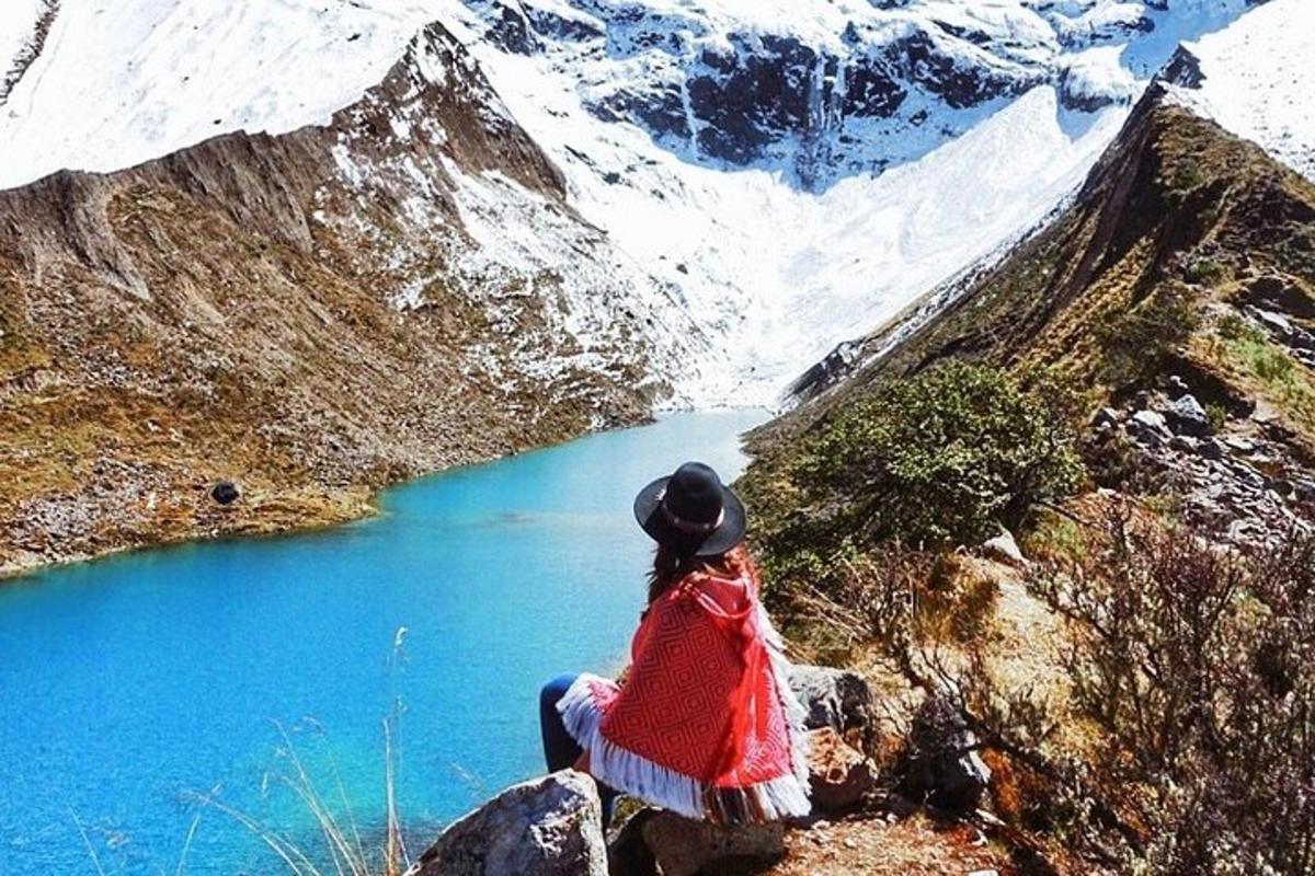 uma mulher sentada no topo de uma montanha olhando para um lago