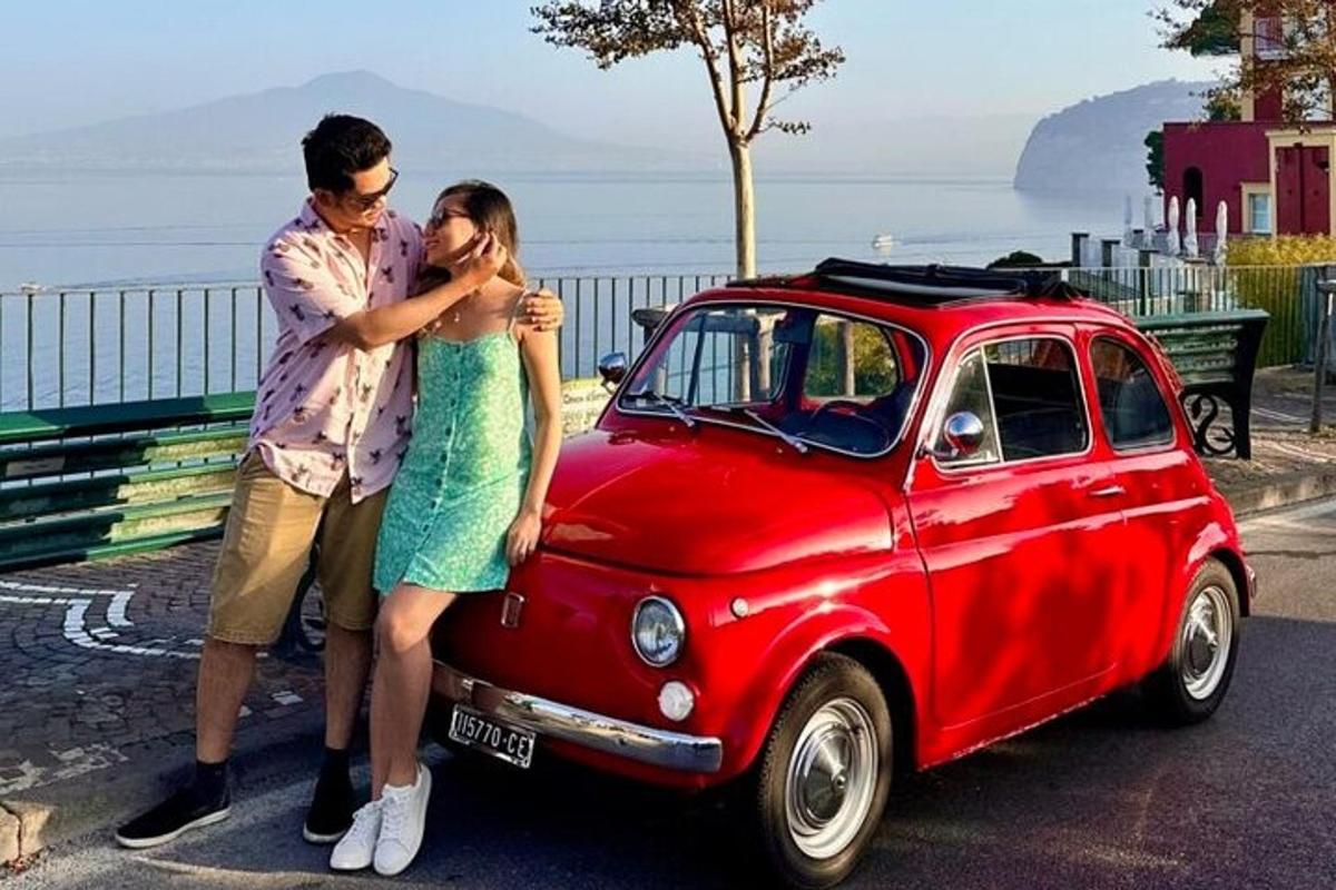 um homem e uma mulher parados ao lado de um carro vermelho