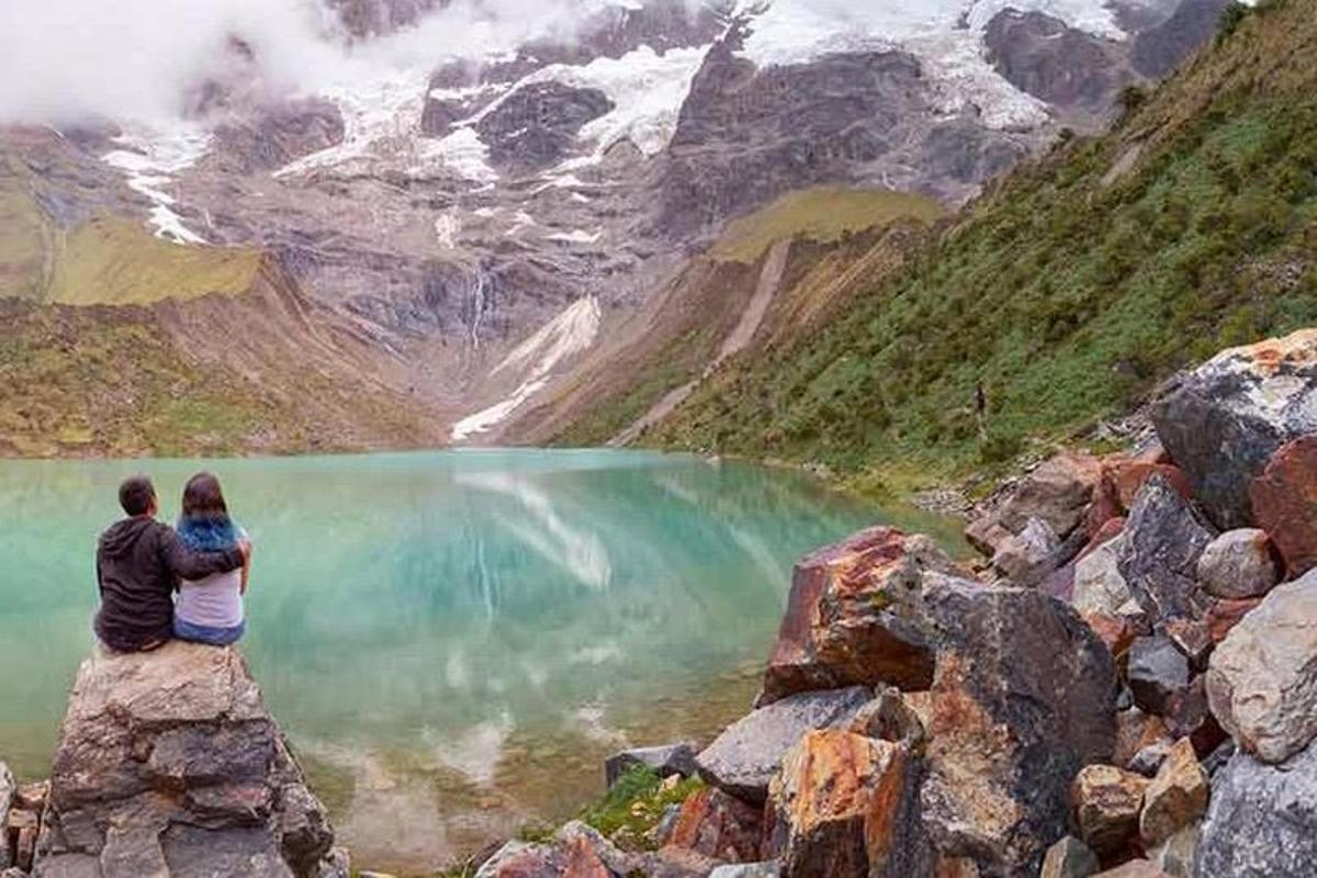moški in ženska sedita na skali s pogledom na jezero