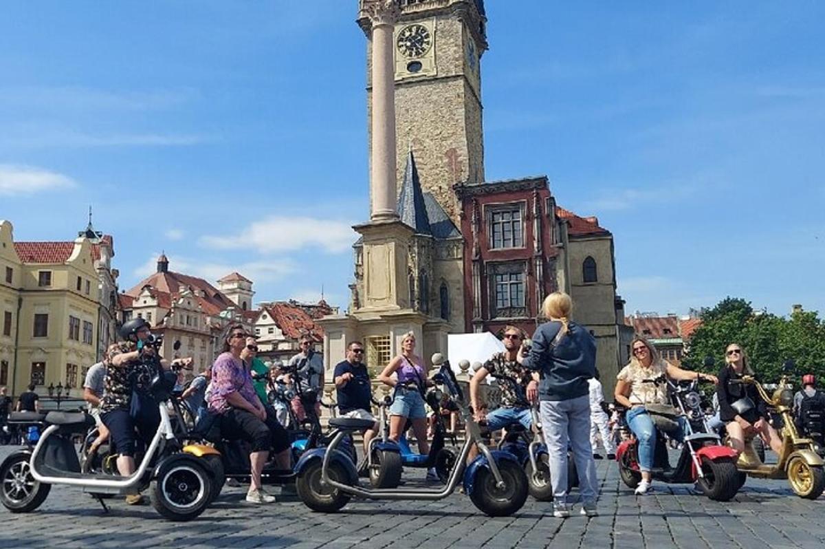 skupina ljudi na skuterjih pred stolpom z uro