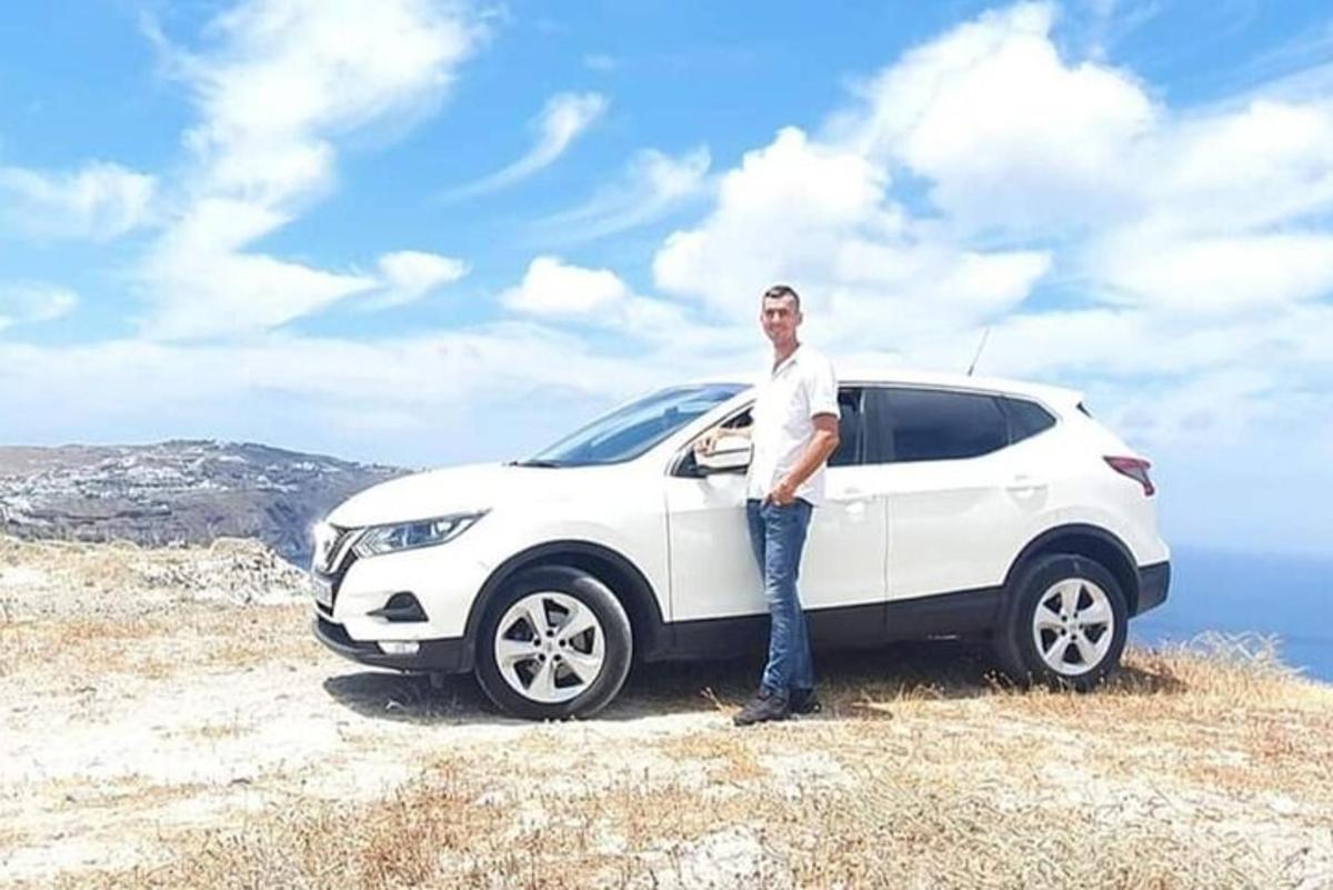 seorang pria berdiri di samping mobil putih di atas bukit