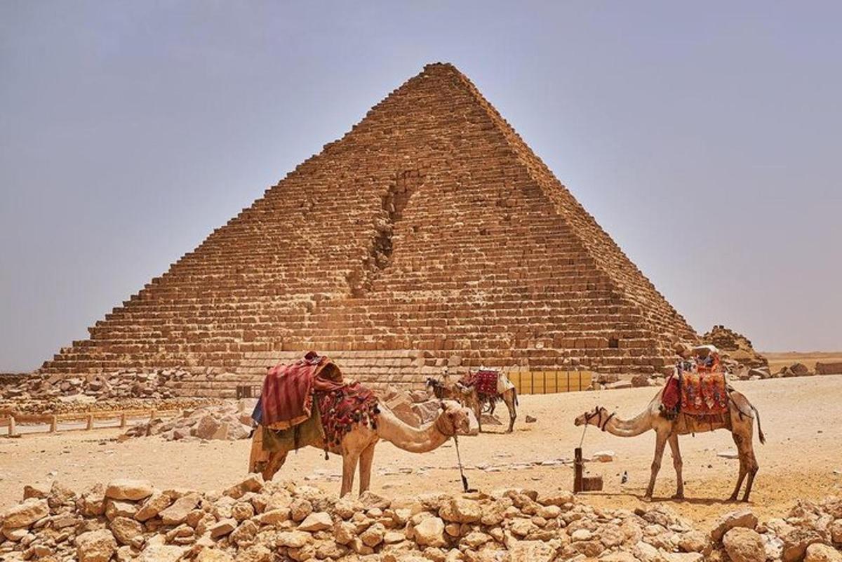 dva lidé na velbloudech před pyramidou