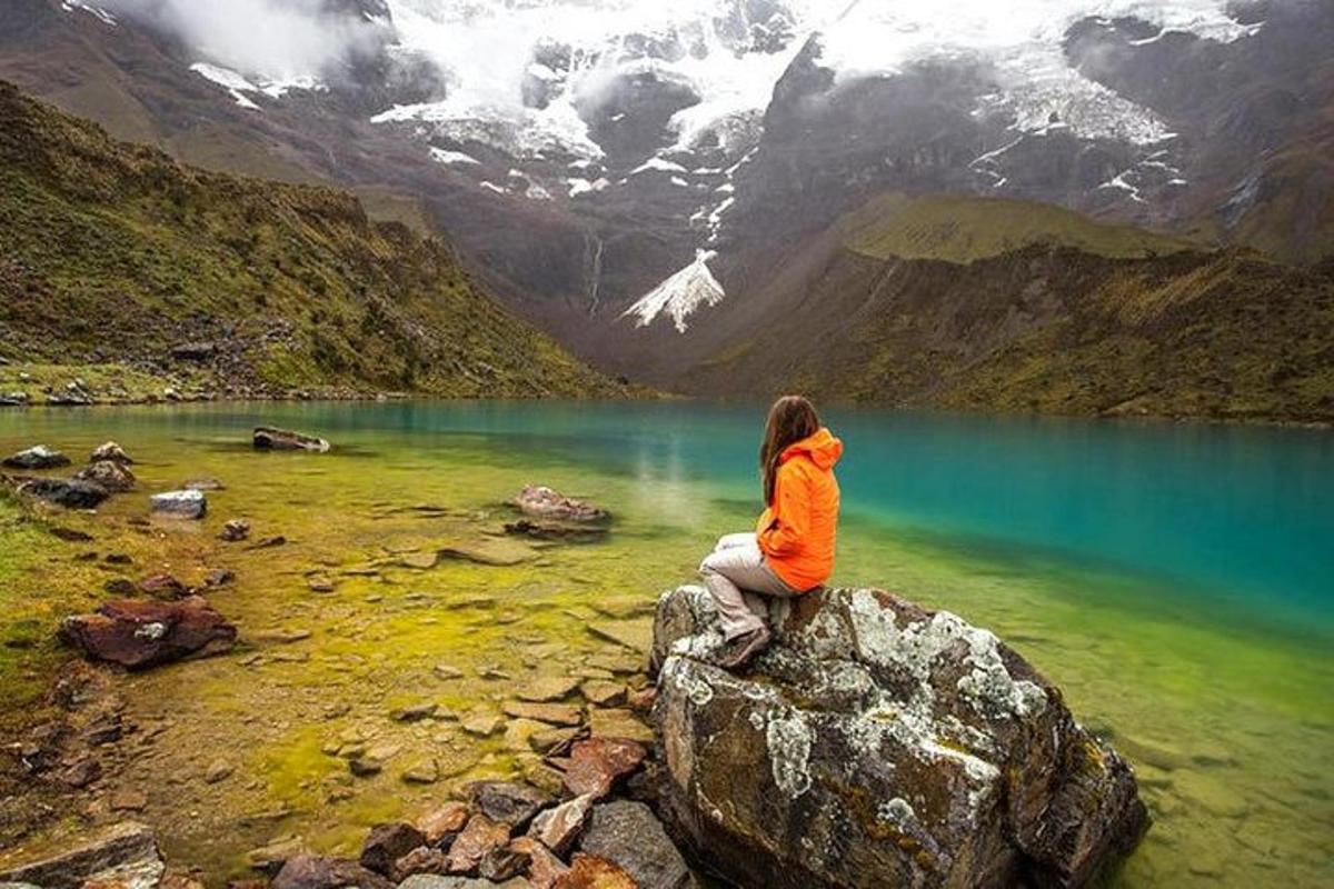 una persona seduta su una roccia che domina un lago di montagna