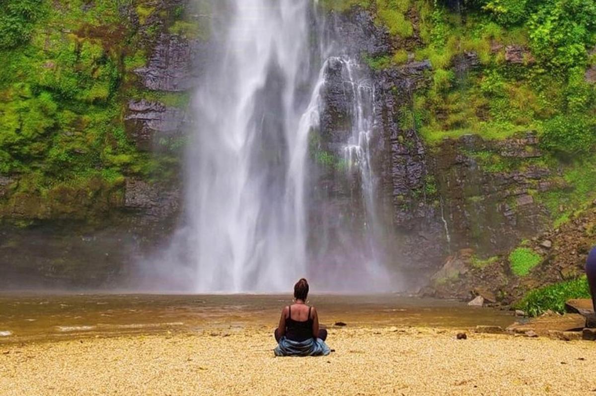 seorang lelaki duduk di pantai di hadapan air terjun
