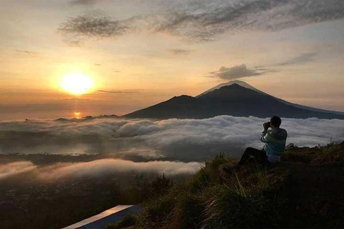 a man sitting on a hill taking a picture of a mountain