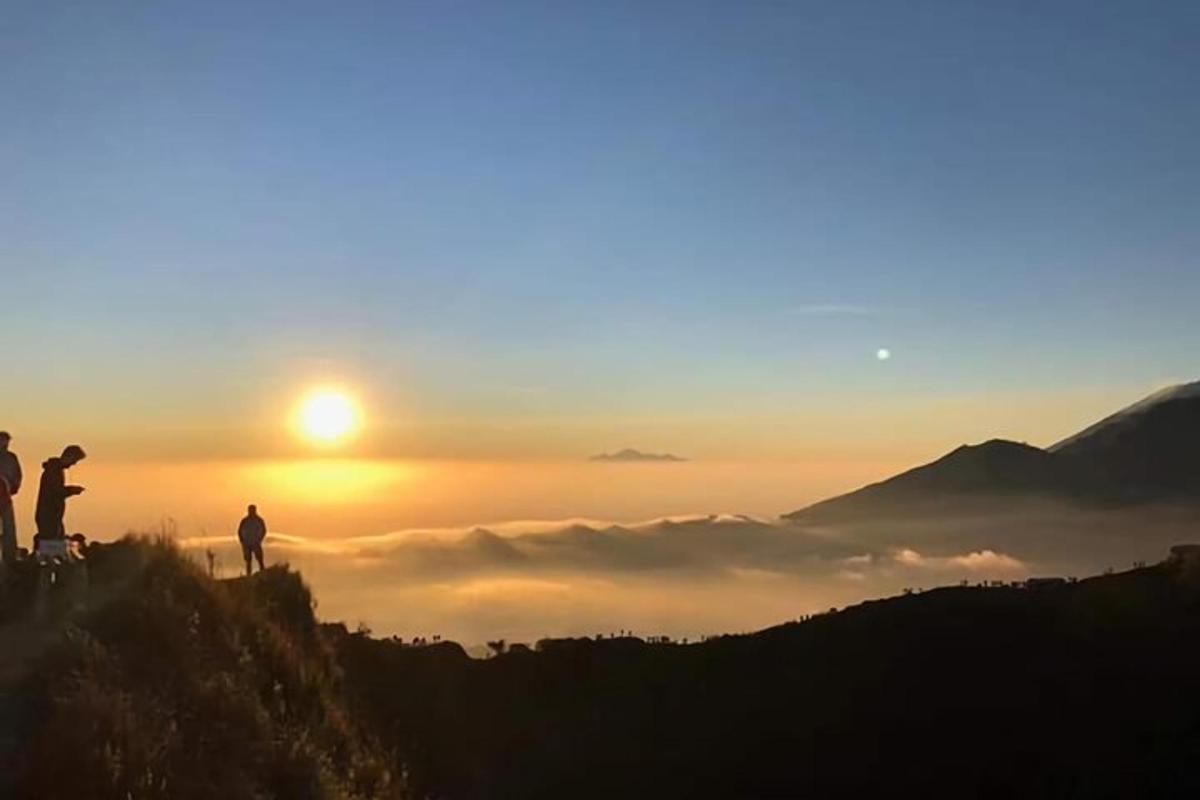 two people standing on top of a mountain at sunset