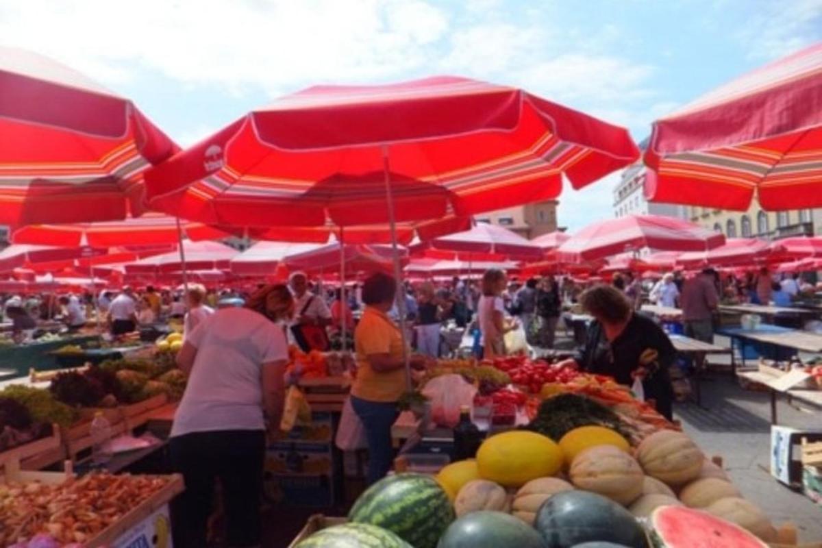 Un grupo de personas de pie en un mercado con paraguas rojos.