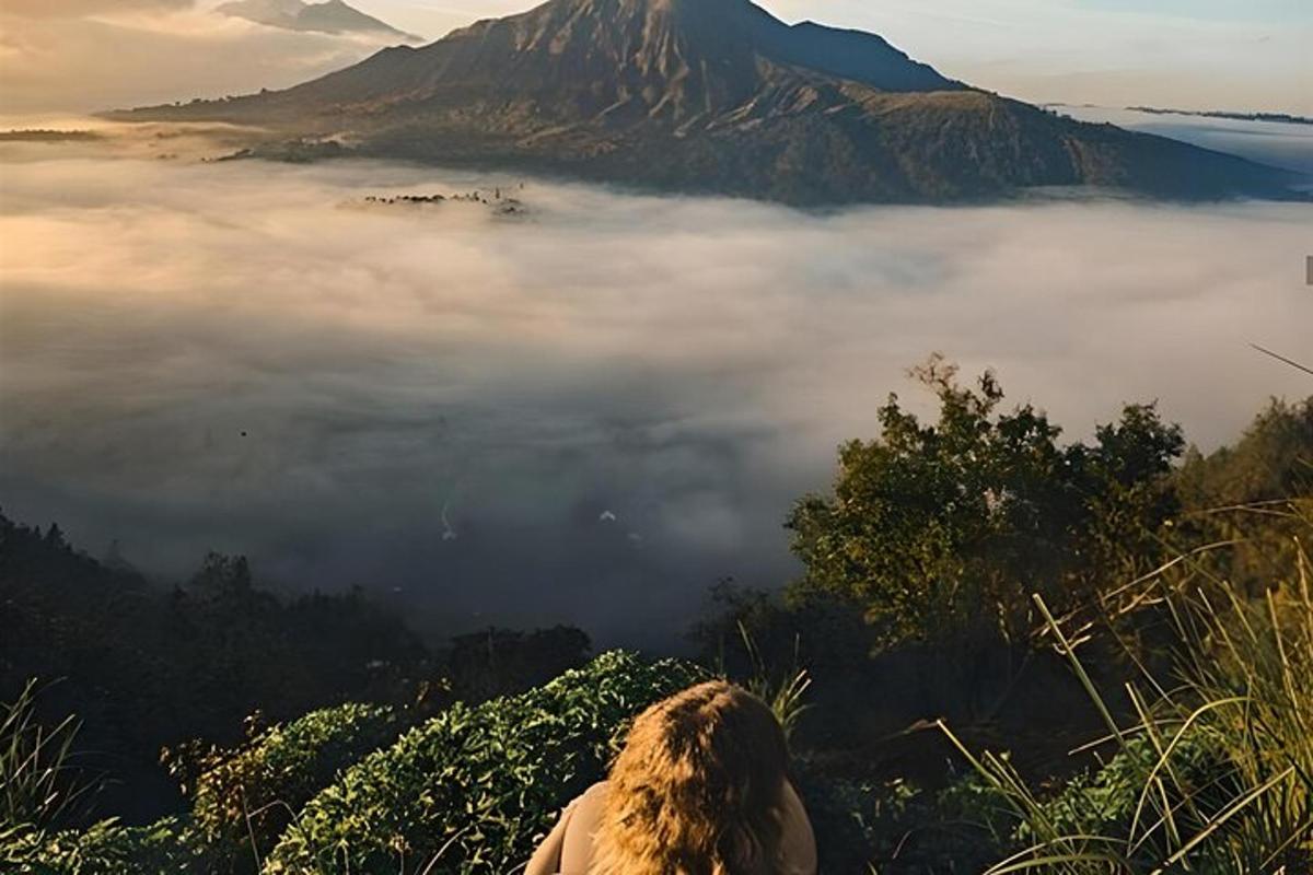 a person sitting on a hill looking at a fog covered mountain