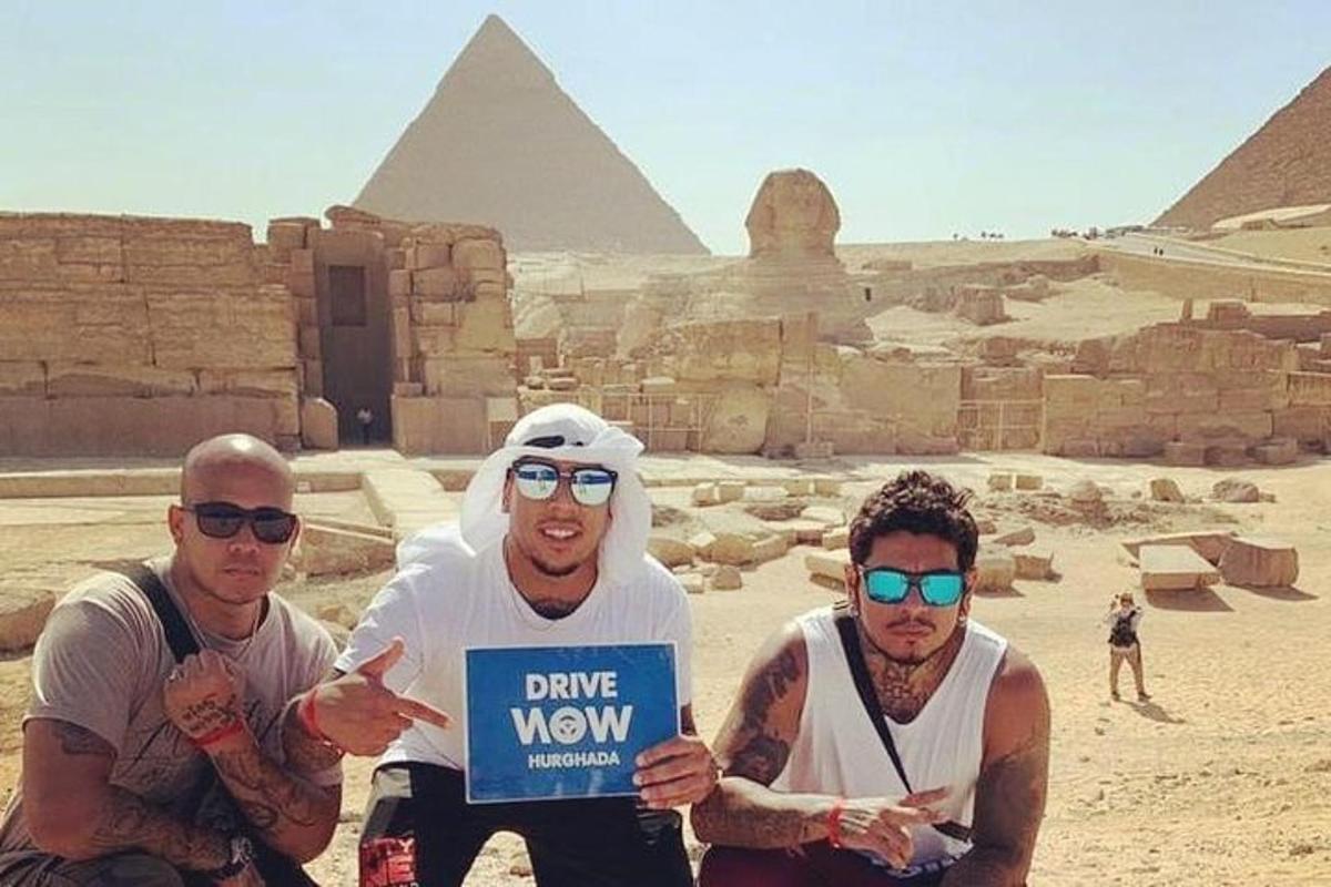 Tres hombres sosteniendo un cartel frente a las pirámides