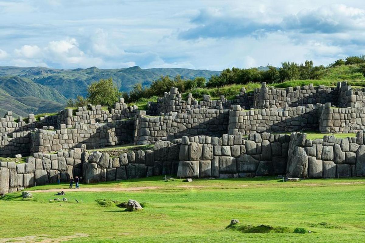 a large stone wall in a field with mountains in the background
