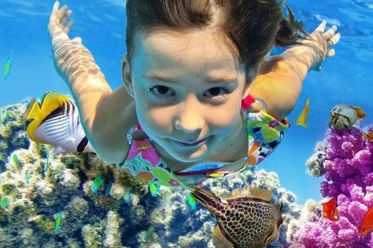 seorang gadis kecil berenang di air bersama seekor ikan