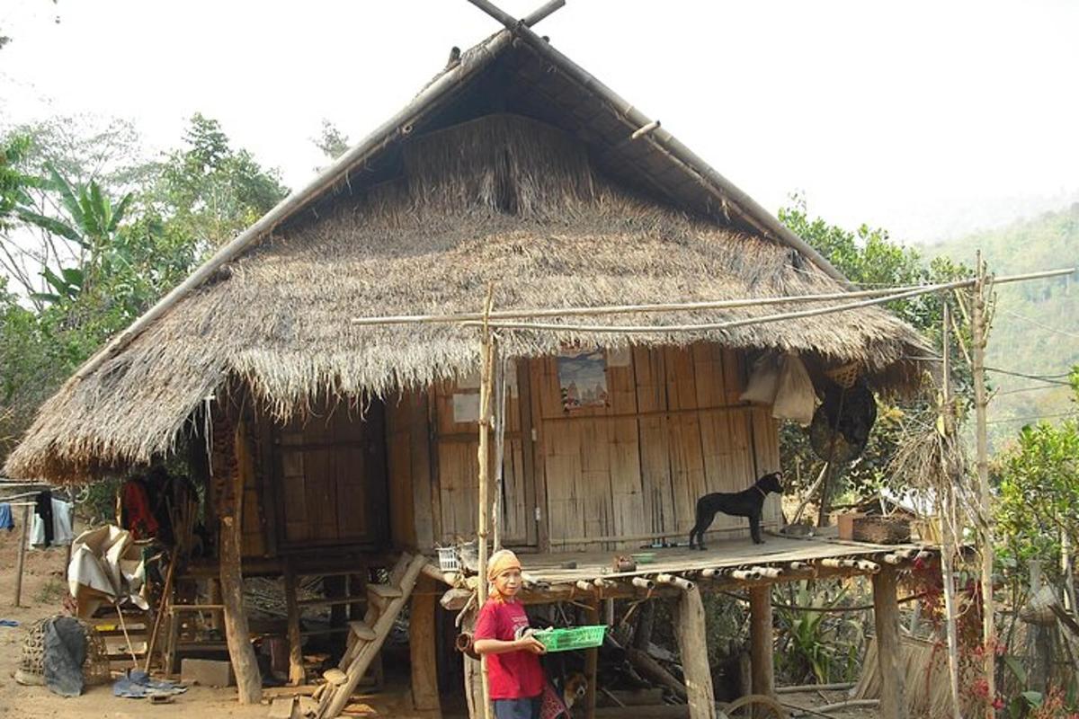 a woman standing in front of a hut with a black cat
