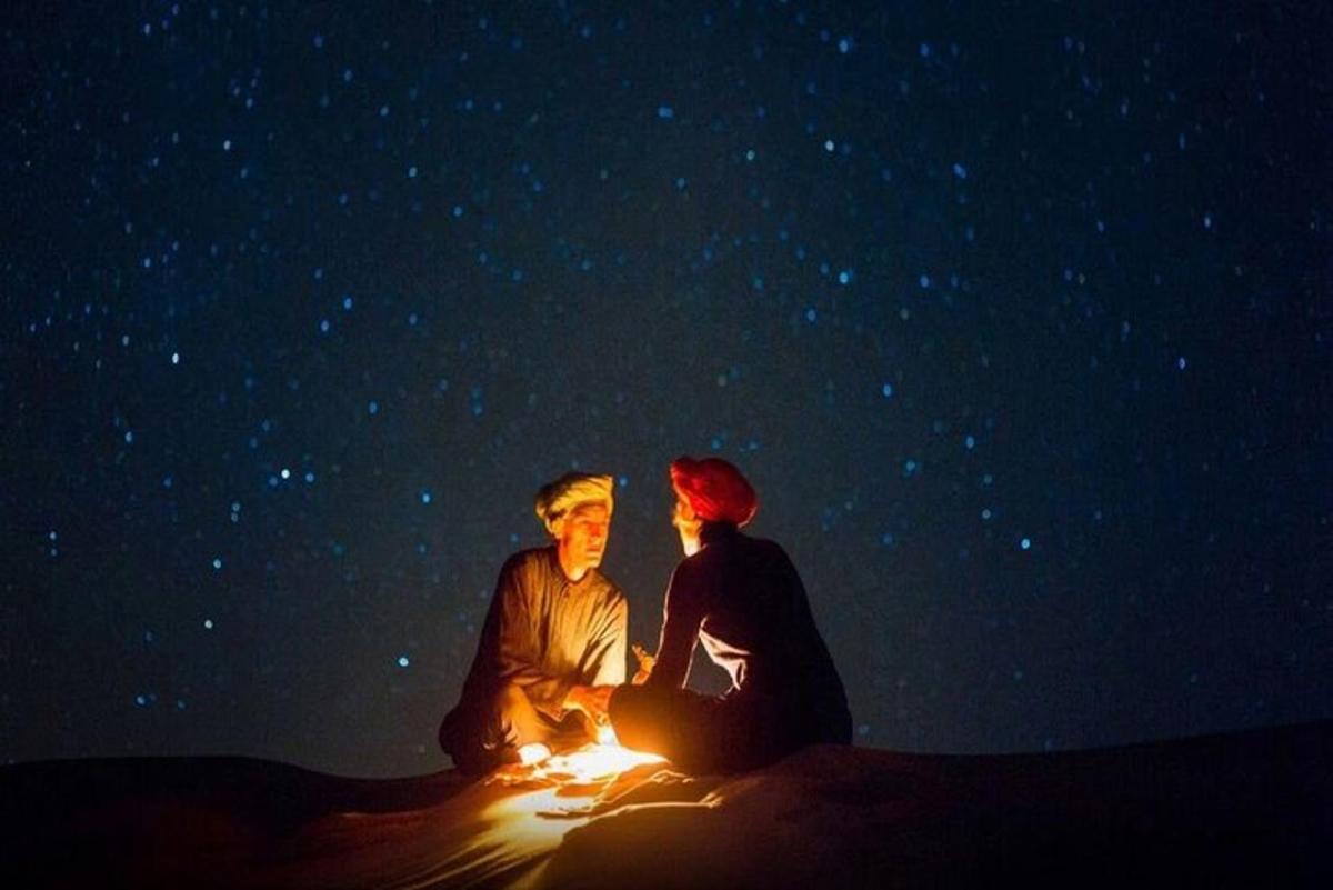 una coppia seduta accanto a un fuoco nel deserto di notte