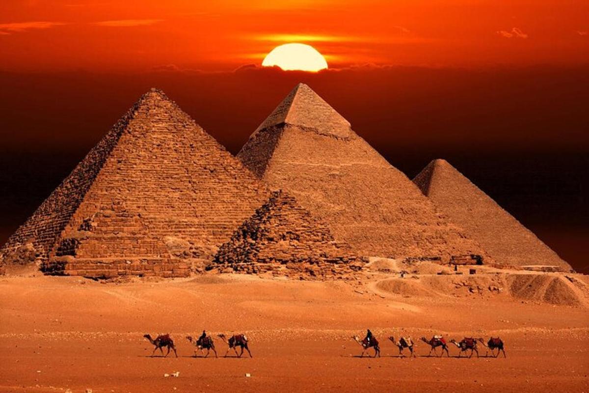 Skupina lidí jedoucích na velbloudech před pyramidami