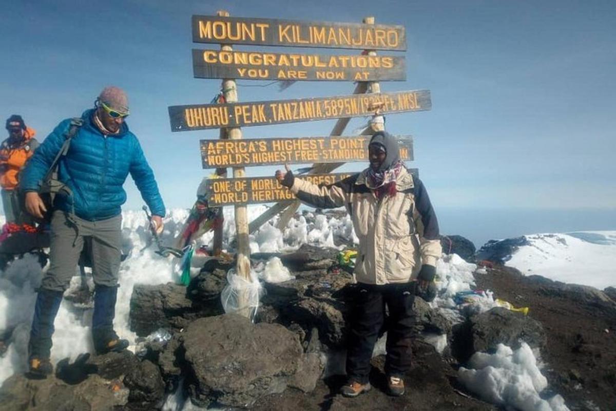 dua lelaki berdiri di sebelah papan tanda di puncak gunung